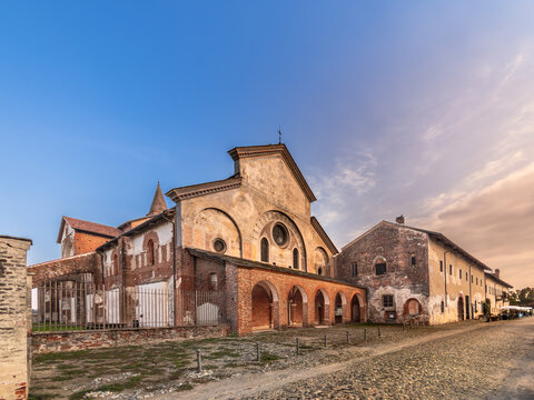Revello, Piedmont, Italy - Santa Maria di Staffarda Abbey. Ancient 12th-century Cistercian monastery Romanesque-Gothic architecture with red brick facades, arches, and cobbled street, colorful sky.