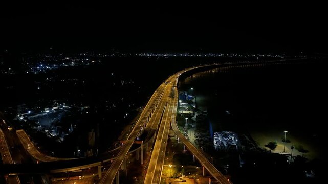 Cinematic aerial drone footage of Atal Setu, also known as Mumbai Trans Harbour Link, illuminated at night, showing the sweeping sea bridge, connecting highways, waterfront and distant city lights.