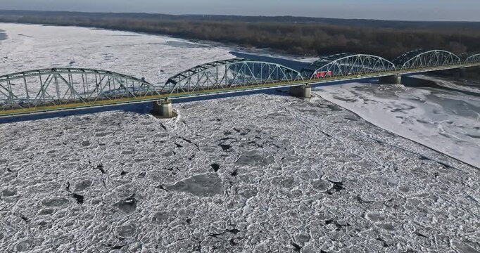 Vehicles crossing a bridge above river covered in ice floes.