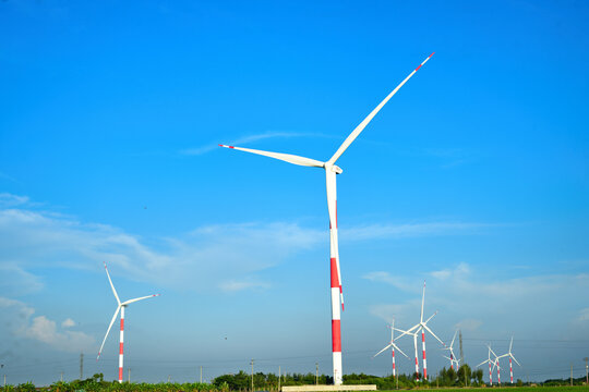 Wind turbines with red and white striped poles generating clean energy in a green field under a clear blue sky.