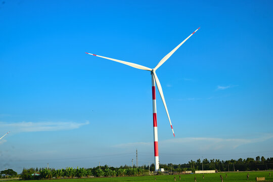 Wind turbines with red and white striped poles generating clean energy in a green field under a clear blue sky.