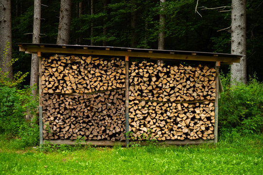 Stacked firewood logs are stored in a covered wooden shed at the edge of a forest in Lauterbrunnen, Switzerland. The outdoor setup highlights natural fuel resources and forestry.