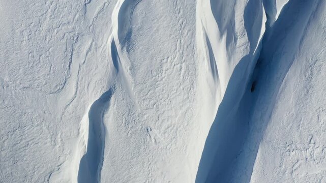 Top-Down Abstract Drone Shot of Curved Snow Ridges and Blue Glacial Shadow Patterns