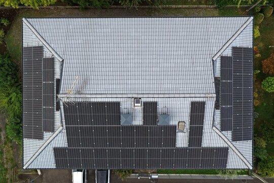 Aerial view of a residential house roof with installed solar panels for renewable energy power. A top down perspective of a tiled roof featuring multiple photovoltaic modules capturing sunlight