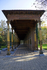 An ornate covered wooden gallery featuring carved timber pillars and decorative cornices lines a park pathway in Tashkent, Uzbekistan © Gregory