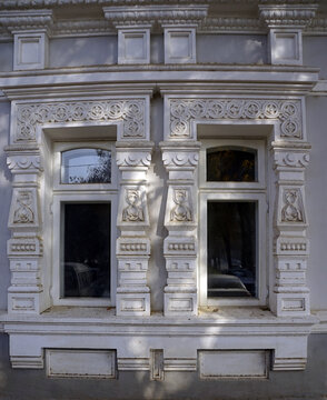 Intricate white carved stucco reliefs and ornamental pilasters frame a pair of historic windows on a Tsarist-era colonial building in Tashkent, Uzbekistan