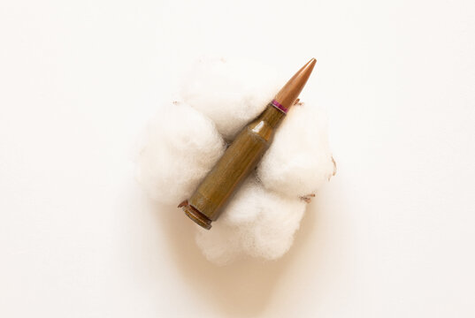 A single bullet resting on white cotton against a white background; a close-up shot themed around weapons
