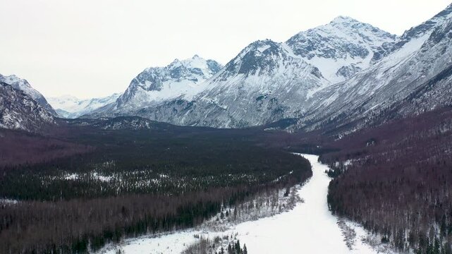 Aerial View of Snowy Winding River Valley and Forested Mountain Range