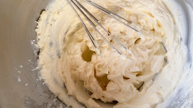 Fresh lemon-colored custard cream whipped with a whisk in a stainless steel bowl, showing its light and airy texture. The close-up baking scene represents homemade desserts, cake preparation