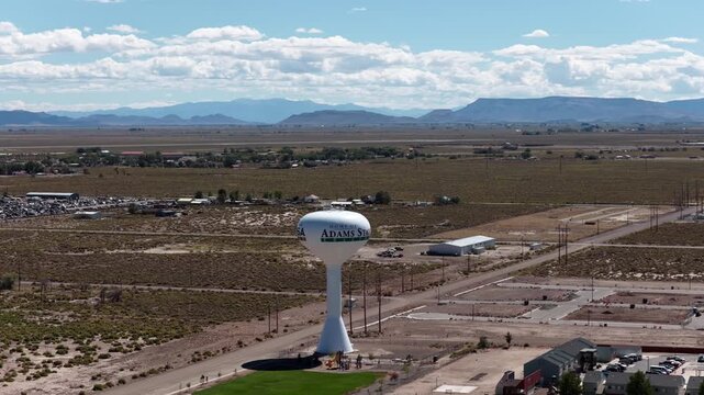Aerial of a white water tower with college logo in a rural landscape near Alamosa Colorado with mountains in the background under a cloudy sky