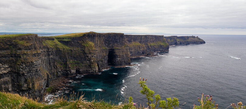 Scenic elevated view of the Cliffs of Moher and Atlantic Ocean with green grassy hill in the foreground, County Clare, Ireland.