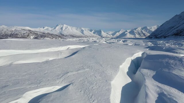 Low-Angle Aerial Flyover Above Textured Snowfield Revealing Alpine Peaks