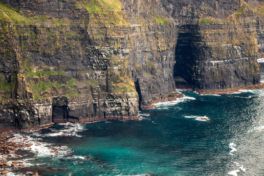 Close-up of massive sea cliffs and deep coastal caves with turquoise ocean water at the Cliffs of Moher, County Clare, Ireland.