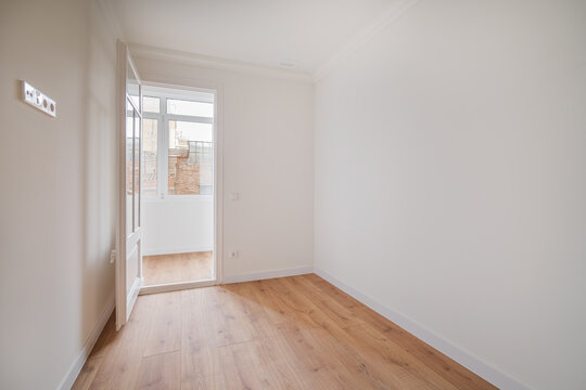 Empty room with white walls and wooden floor. A door is open, leading to a bright area with natural light.