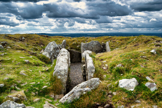 Open megalithic passage tomb and standing stones under moody sky at Loughcrew County Meath Ireland
