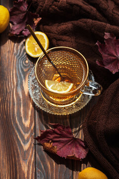 Warm cup of tea with lemon slice and autumn leaves on rustic wooden surface