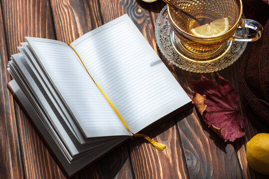 Open lined notebook with yellow bookmark next to a glass of tea and autumn leaf on wooden table