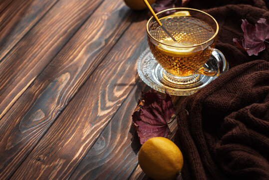 Warm cup of herbal tea with lemon slice and brown scarf on rustic wooden table