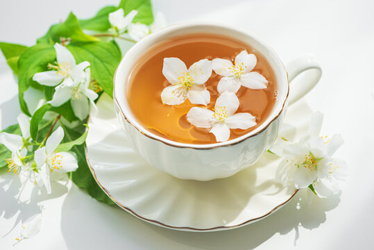 White teacup filled with jasmine tea and delicate white flowers floating on top