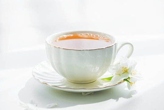 Still life of a white porcelain teacup filled with amber tea and delicate white jasmine flowers on a saucer