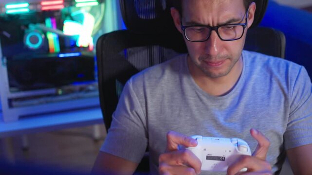 Adult man reacting with game controller during intense gameplay at glowing PC desk, side view with colorful RGB light reflections and focused expression