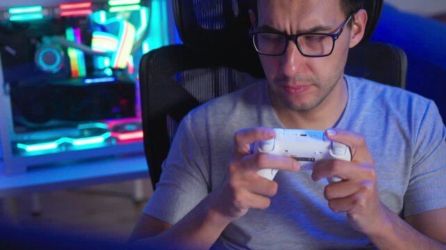 Adult man reacting with game controller during intense gameplay at glowing PC desk, side view with colorful RGB light reflections and focused expression