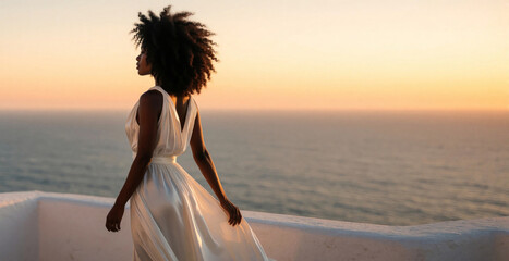 Obraz premium Elegant African American woman in white silk dress stands on Mediterranean balcony. Young black lady looks at sunset over blue ocean. Serene view of sea horizon during golden hour. Peaceful solo
