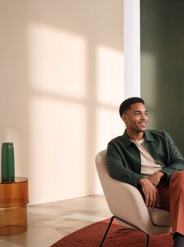 Smiling young African American man sitting in modern armchair. Happy male resting indoors. Stylish home interior