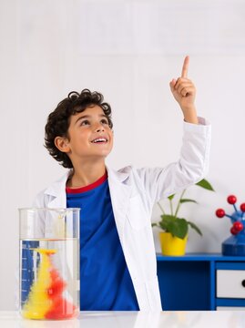 Happy schoolboy in lab coat pointing up during chemistry experiment. Young boy discovering science idea with colorful beaker