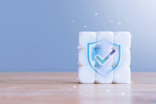 Glowing security shield icon with checkmark overlay on white cubes grid on wooden table. Cyber security, data protection, business insurance, compliance and trust approval concept.