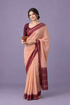 Elegant woman wearing peach saree holding clay lamp against lavender background for durga puja with navratri and diwali traditional festive fashion themes