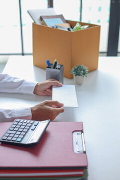 Office worker handing over an envelope, next to a packing box filled with personal belongings. Concept for resignation or leaving a job.