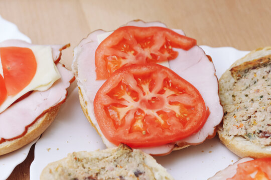 Open sandwiches with ham tomato. Fresh tomato slices on ham. Bread rolls with savory toppings. Homemade lunch preparation. Colorful snack ingredients. Food background with prepared sandwiches.