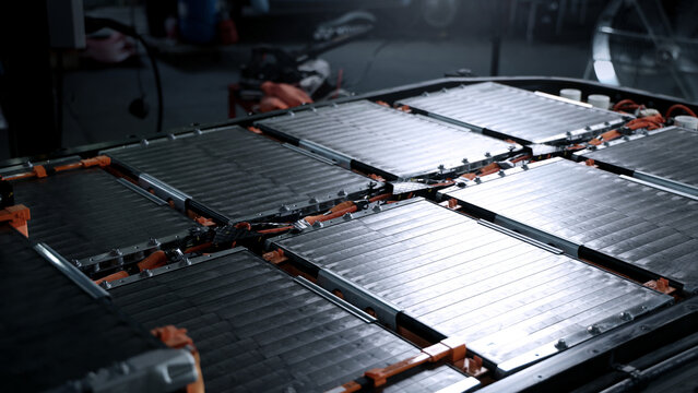 EV car service. Electric vehicle battery pack being serviced or inspected in automotive workshop. Large battery modules and high voltage components. Modern EV power systems. Lithium ion NMC NCA or LFP