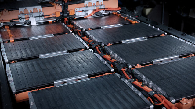 EV car service. Electric vehicle battery pack being serviced or inspected in automotive workshop. Large battery modules and high voltage components. Modern EV power systems. Lithium ion NMC NCA or LFP