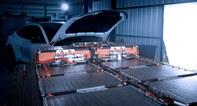 EV car service. Electric vehicle battery pack being serviced or inspected in automotive workshop. Large battery modules and high voltage components. Modern EV power systems. Lithium ion NMC NCA or LFP