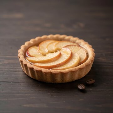 individual mini glazed apple tartlet with spiral apple slices on dark wooden table with scattered roasted coffee beans