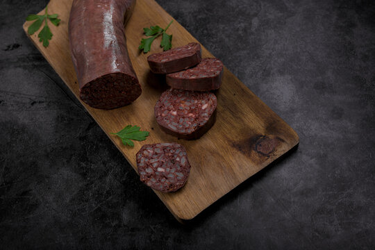 Sliced Spanish morcilla blood sausage on wooden board with parsley garnish over dark slate background, rustic traditional food overhead view