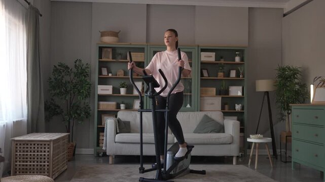 Young woman training at home on elliptical machine