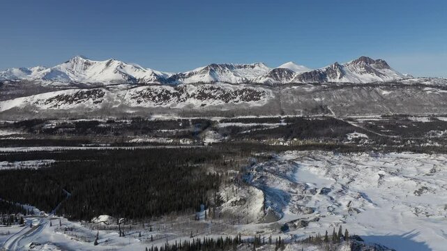 High Aerial Descent Over Snowy Forest Valley Toward Mountain Range