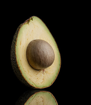 A single ripe avocado half with a large central pit isolated against a deep black background