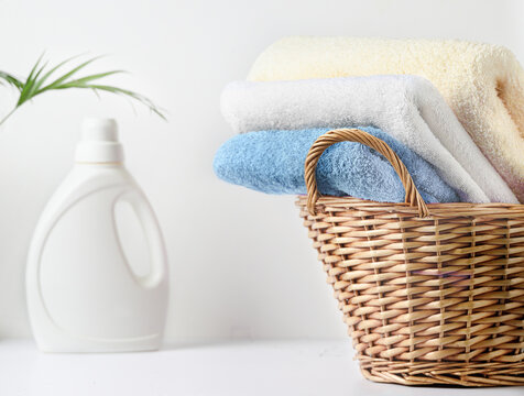 Stacked pastel towels in wicker basket beside laundry detergent bottle on white countertop linen set