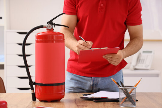 Fire safety inspection and compliance, technician checking fire extinguisher equipment with clipboard in office for building maintenance and regulation