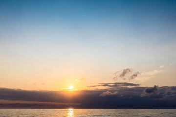 Fototapeta premium setting sun in dark sky over low clouds and sea