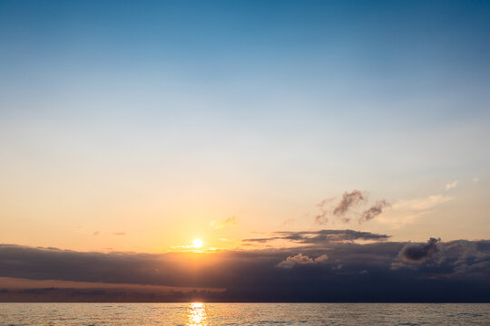 setting sun in dark sky over low clouds and sea