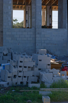 Stacked cinder blocks and construction materials sit in front of a partially built concrete block structure, suggesting masonry work, building progress, labor and residential development at an outdoor
