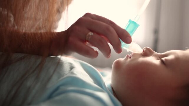 Extreme close up of mother removing thick nasal mucus from baby with aspirator. Dry lips and heavy congestion suggest childhood illness after daycare.