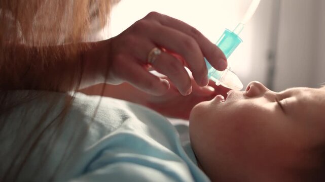 Mother carefully removes stubborn nasal mucus from unhappy baby with aspirator. Slow motion close up reveals active congestion during childhood illness.