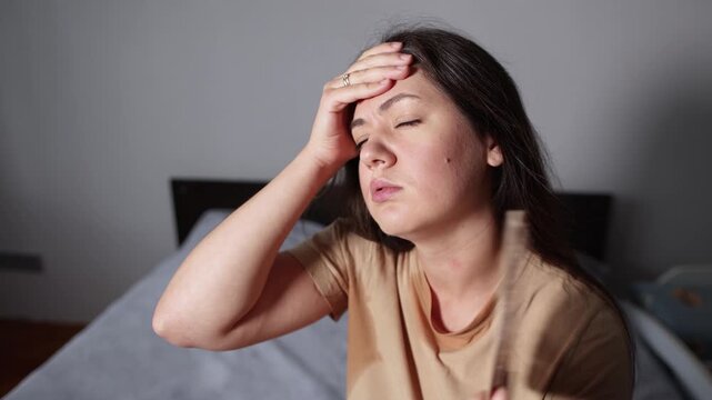 Young woman holds her hot forehead while sweating through her shirt. Slow motion footage portrays exhaustion and physical stress during oppressive summer heat.