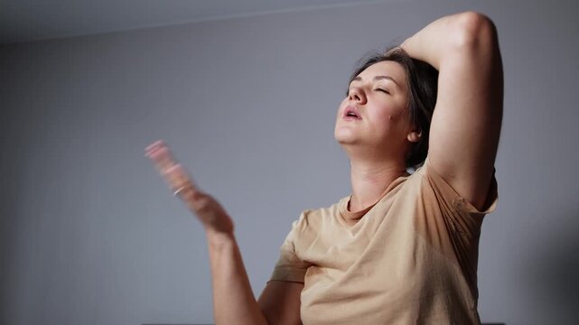 Young woman lifts her hair and waves her hand against her face and neck. Slow motion footage shows sweating and discomfort without air conditioning or fan.